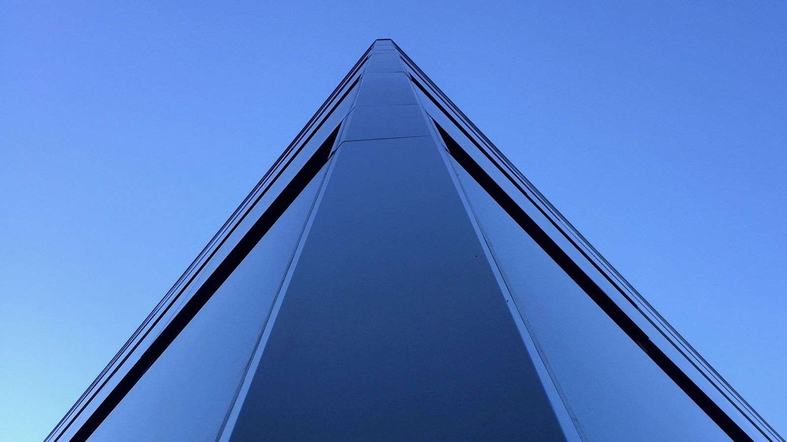 The edge of a glass tower rising to a point against a clear blue sky