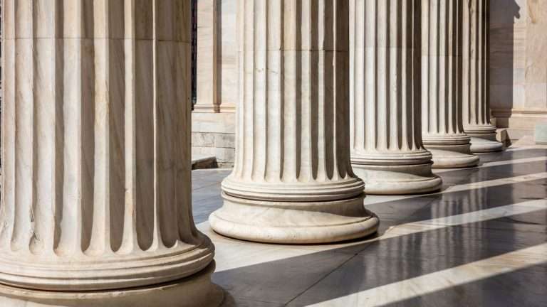 A row of fluted marble columns casting shadows across a stone floor